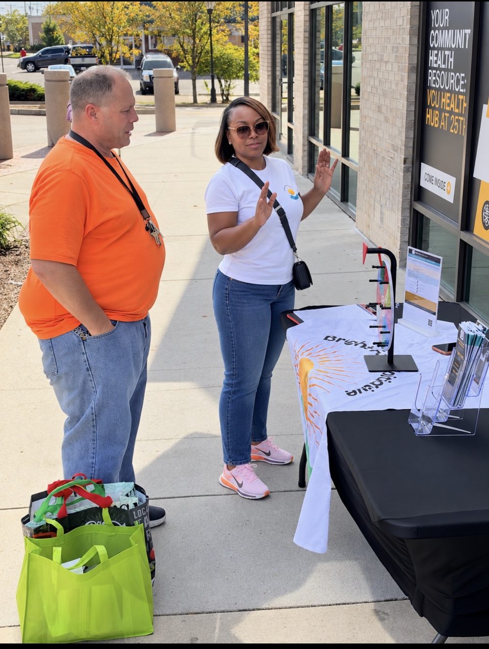 Two people talking at the Bright Focus Initiative 804 outreach table outside the VCU Health Hub at 25th, with the prize wheel on the table