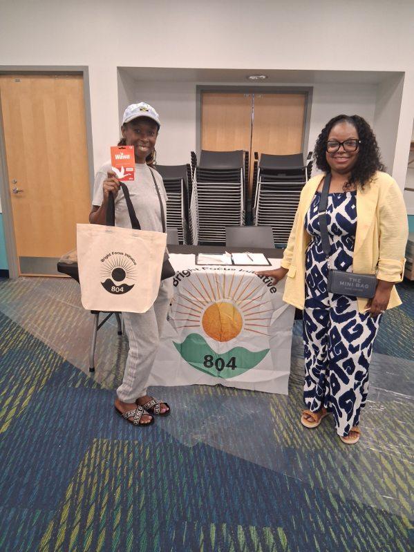Community member holding a Bright Focus Initiative 804 tote bag and gift card next to a volunteer at the branded table