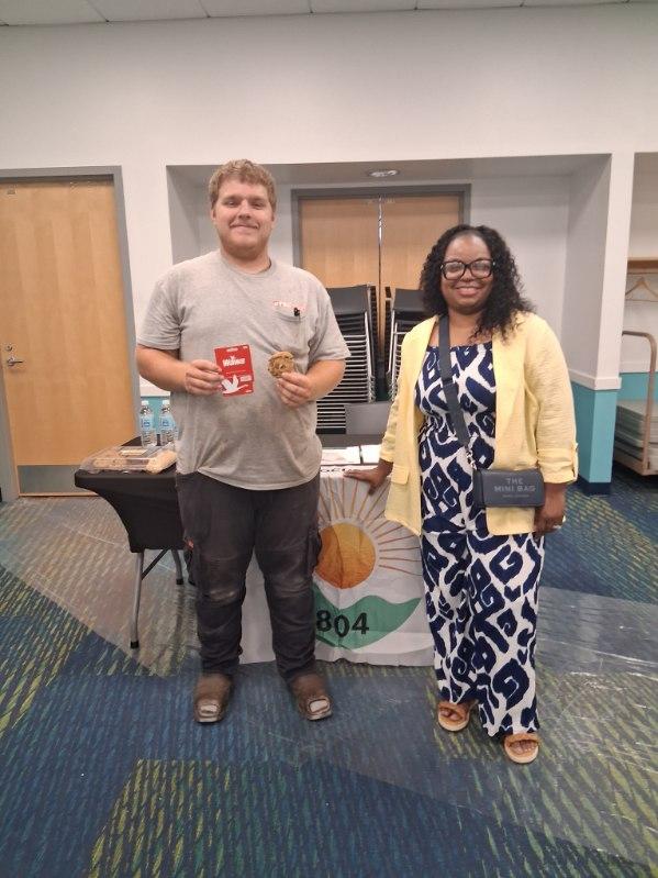 Recipient holding a gift card and cookie beside a volunteer in front of the Bright Focus Initiative 804 banner
