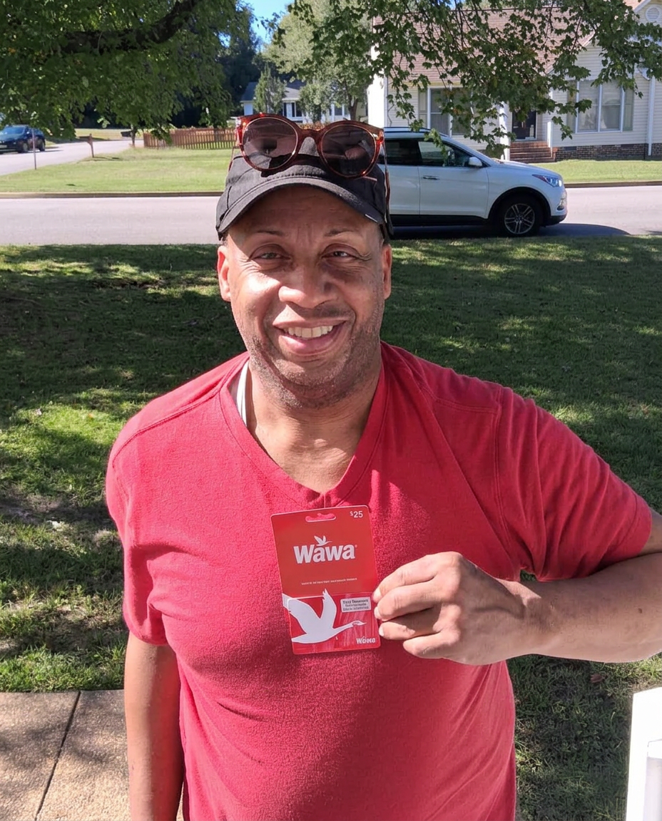 Smiling community member in a red shirt holding a Wawa fuel gift card